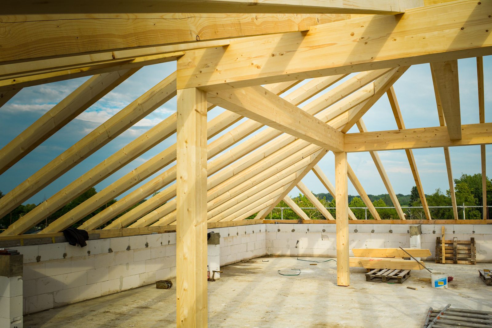 Neu aufgerichteter Dachstuhl aus Holz mit Sparren, Pfetten und Stützen auf einem gemauerten Rohbau, darüber Himmel