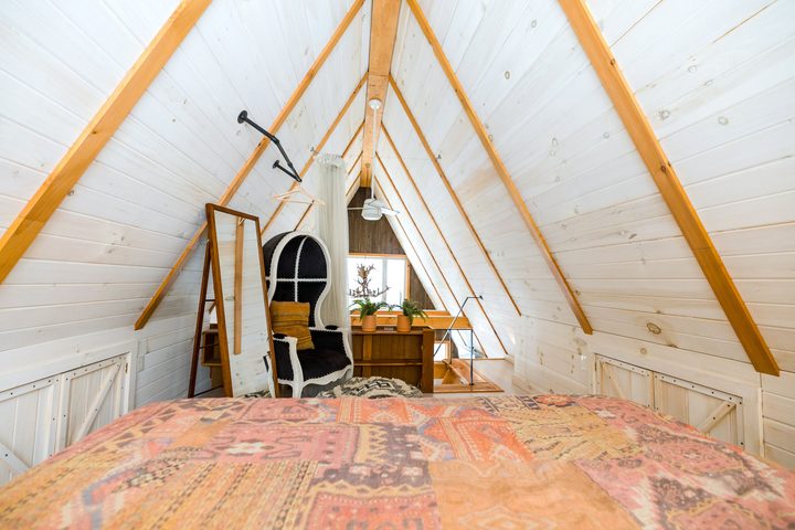 Ausgebautes Dachgeschoss mit heller Holzverschalung, sichtbaren Sparren, Sessel und Bett