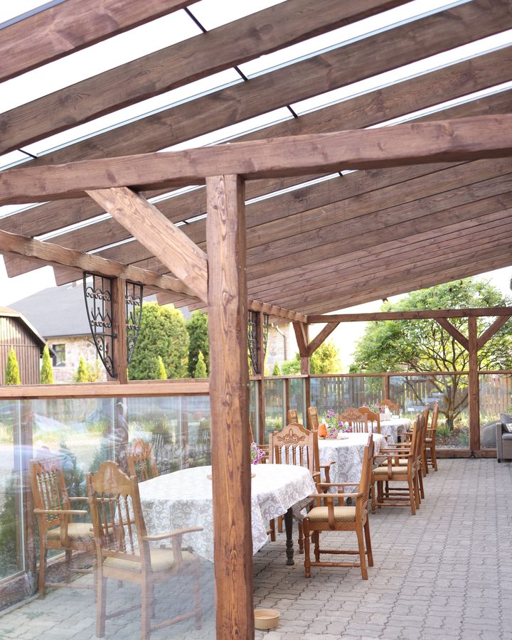 Überdachte Terrasse mit Holzpfosten, Kopfbändern und Sparren, darunter gedeckte Tische