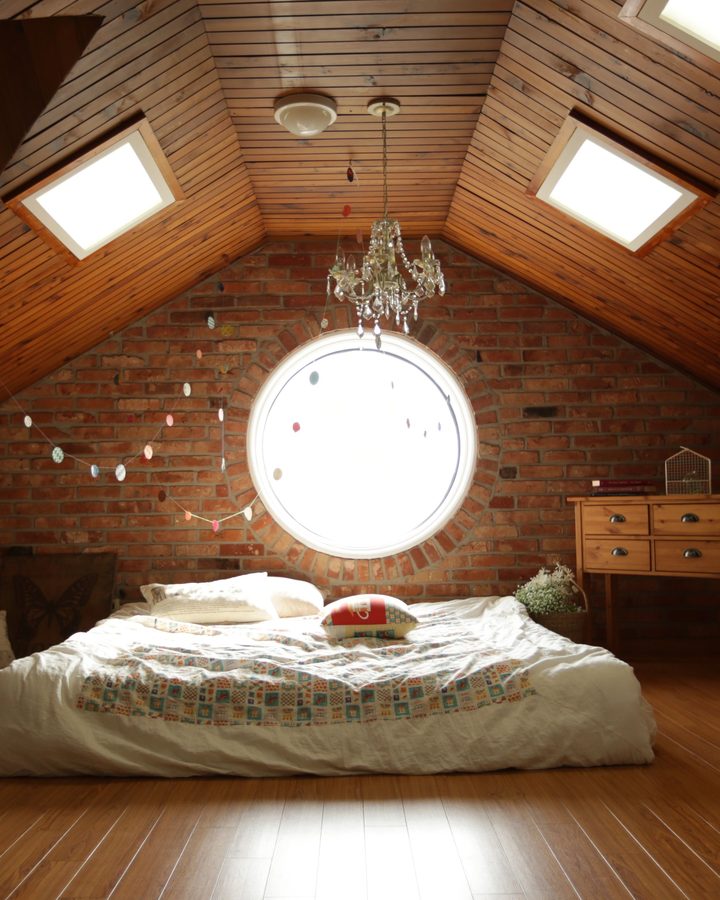 Dachgeschosszimmer mit holzverkleideter Schräge, zwei Dachfenstern, Rundfenster und Bett