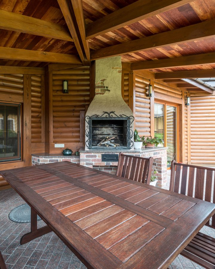 Überdachte Terrasse mit sichtbarer Holzbalkendecke, gemauertem Grillkamin und Holztisch mit Bänken