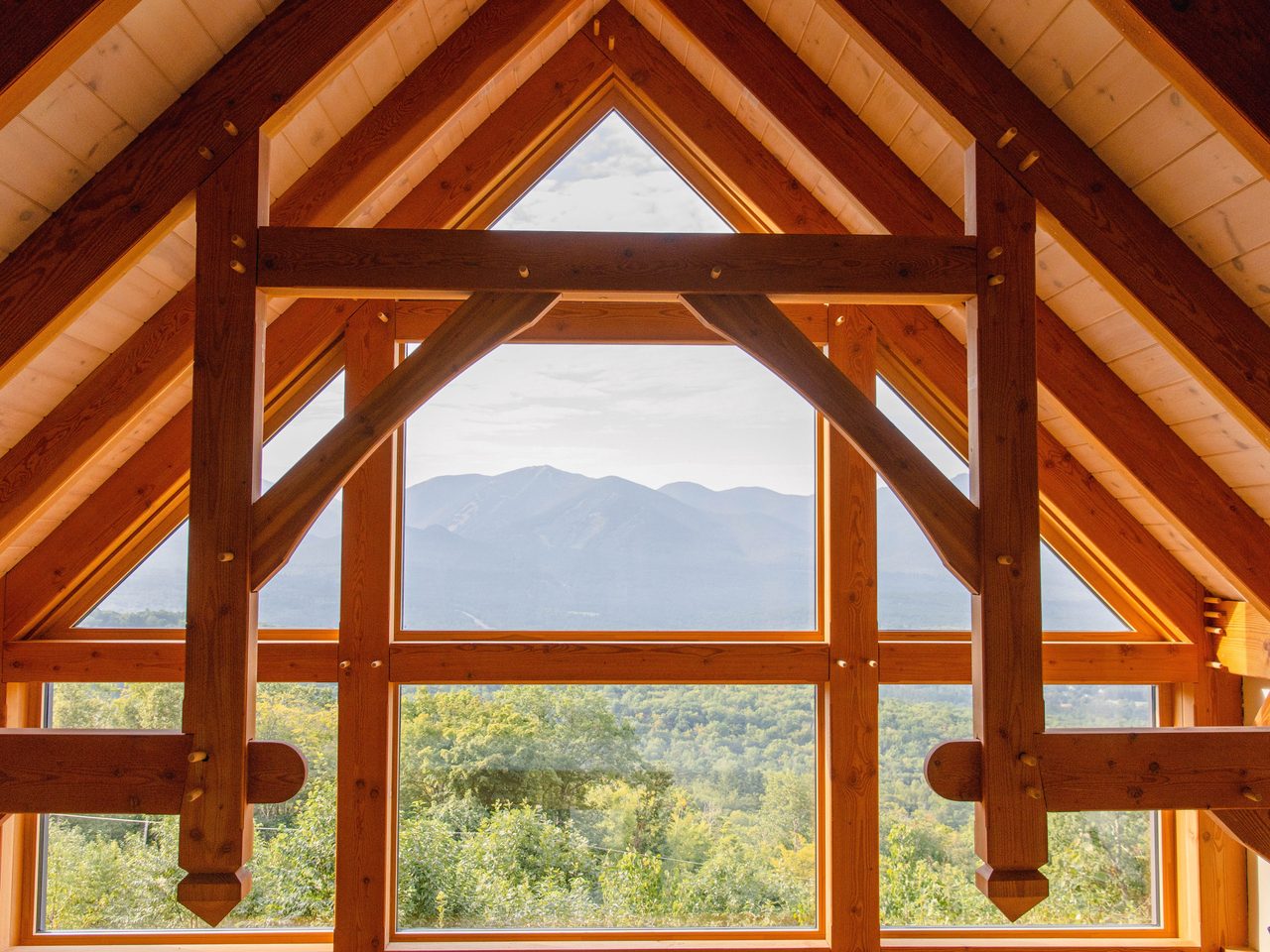 Innenraum mit sichtbarem Holzdachstuhl, Holznägeln und großem Giebelfenster mit Blick auf Berge