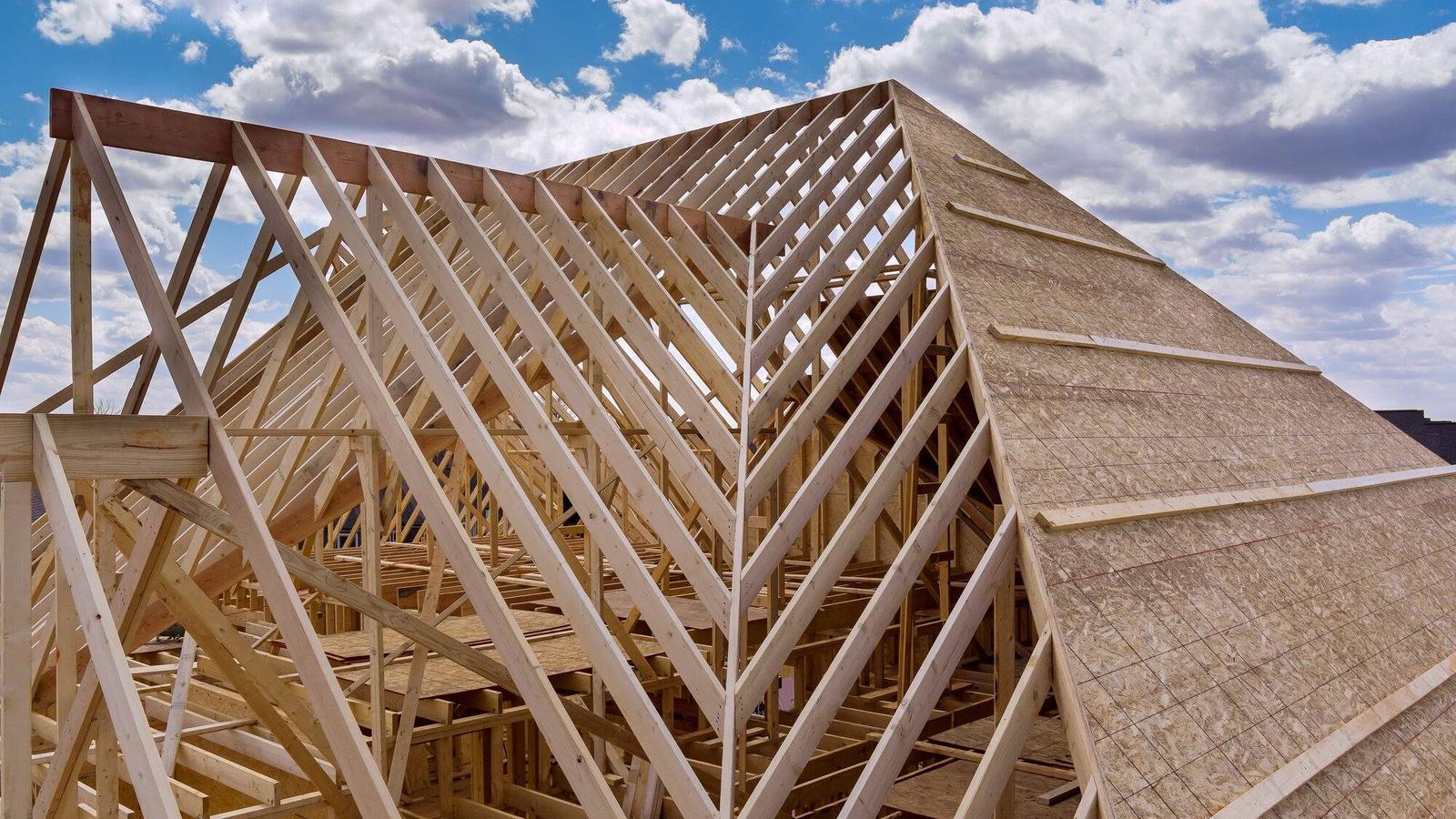 Großer Dachstuhl mit vielen Sparren, teils schon mit Holzwerkstoff-platten beplankt, vor Wolkenhimmel