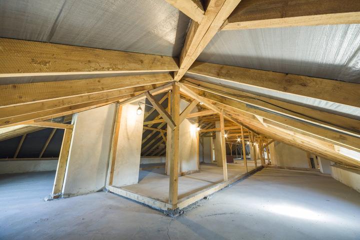Dachgeschoss im Ausbau mit ersten Trennwänden unter den Sparren, beleuchtet von Baustellenlampen