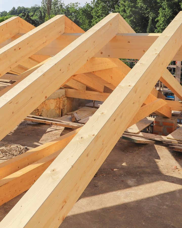 Neuer Dachstuhl mit Sparren auf Pfetten und Stützen über einem Rohbau, im Hintergrund Bäume