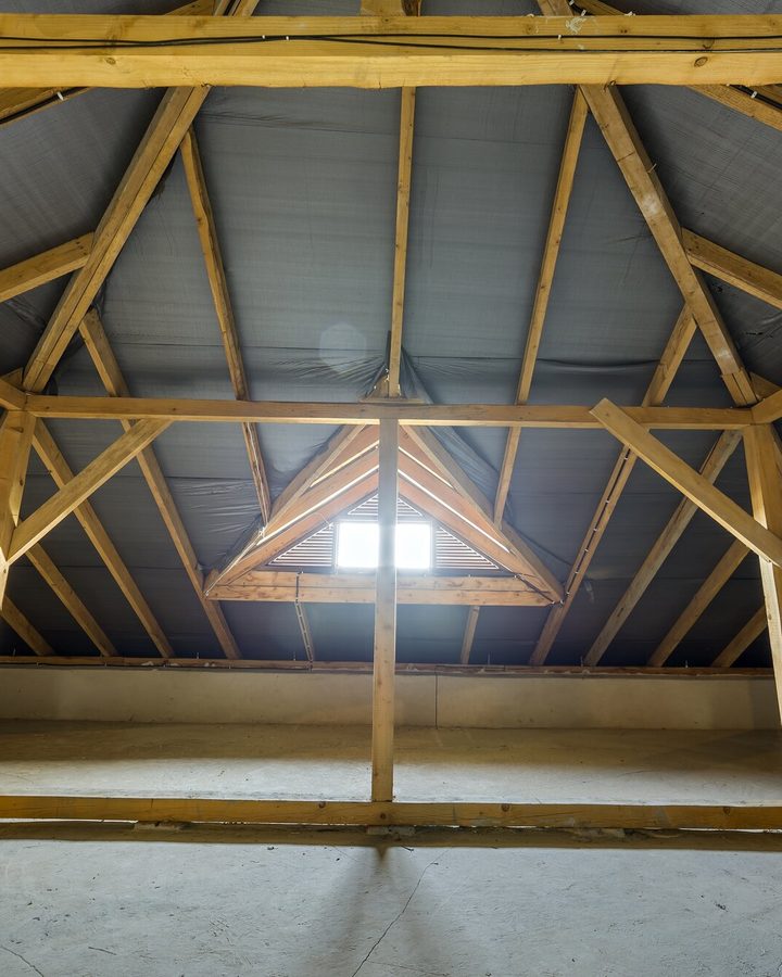 Dachraum mit Kehlbalken und Streben, hinten ein dreieckiges Giebelfenster