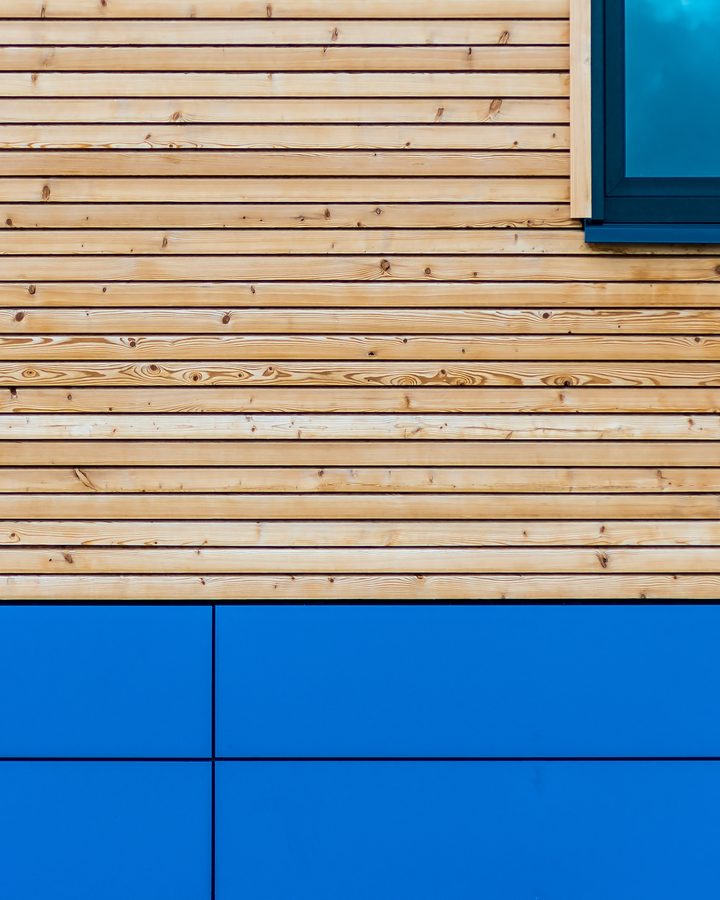 Waagerechte Lärchenschalung mit offener Fuge und einem Fenster, darunter blaue Fassadenplatten
