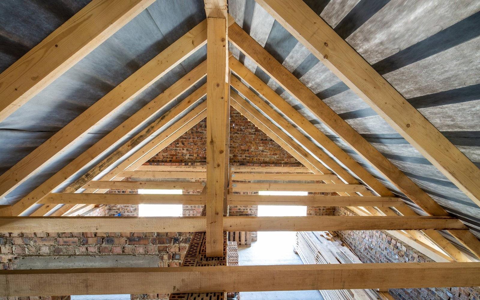 Offener Dachraum mit Sparren, Kehlbalken und Stützen aus hellem Holz, an den Giebeln Ziegelmauerwerk
